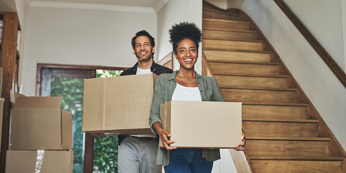 Happy couple holding moving boxes on moving day smiling in new home