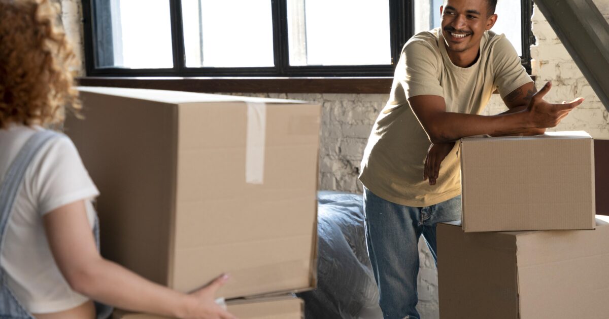 Happy couple handling cardboard boxes together moving into new home smiling