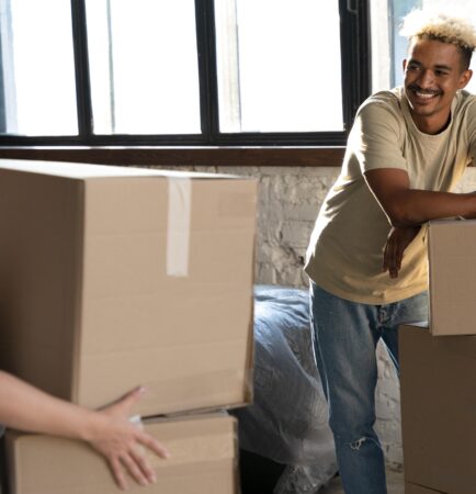 Happy couple handling cardboard boxes together moving into new home smiling